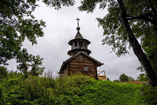wooden ancient church on the island among the trees during the rain - Фото, изображение