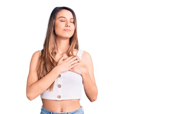 Young beautiful girl wearing casual sleeveless t shirt smiling with hands on chest with closed eyes and grateful gesture on face. health concept.  - Photo, Image