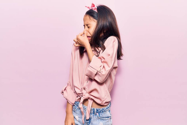 Beautiful child girl wearing casual clothes smelling something stinky and disgusting, intolerable smell, holding breath with fingers on nose. bad smell  - Photo, Image