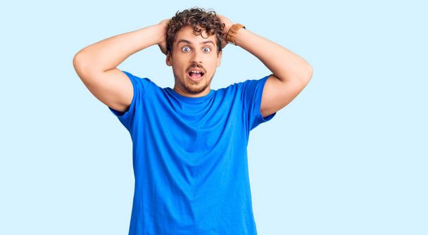 Young handsome man with curly hair wearing casual clothes crazy and scared with hands on head, afraid and surprised of shock with open mouth  - Photo, Image
