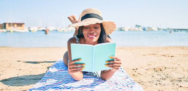 Jovem afro-americana de férias deitado no livro de leitura de toalhas na praia - Foto, Imagem