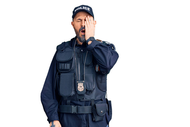 Mladý pohledný muž v policejní uniformě, unaveně zírající a zakrývající půlku obličeje, oko a ústa rukou. bolest v obličeji.  - Fotografie, Obrázek