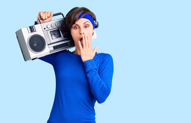 Beautiful young woman with short hair wearing workout clothes and holding boombox covering mouth with hand, shocked and afraid for mistake. surprised expression  - Foto, immagini