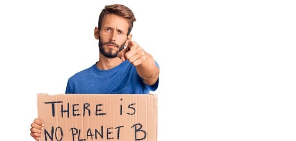 Handsome blond man with beard holding there is no planet b banner pointing with finger to the camera and to you, confident gesture looking serious  - Photo, Image
