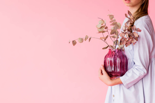 Dívka v modrých lněných šatech pózuje na růžovém pozadí. Dívka drží fialovou skleněnou vázu se suchými rostlinnými větvemi v rukou. Vodorovná fotografie - Fotografie, Obrázek