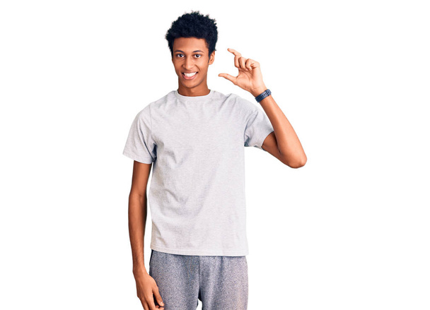 Giovane uomo afroamericano indossa abiti casual sorridente e fiducioso gesticolando con mano facendo segno di piccole dimensioni con le dita guardando e la fotocamera. concetto di misura.  - Foto, immagini