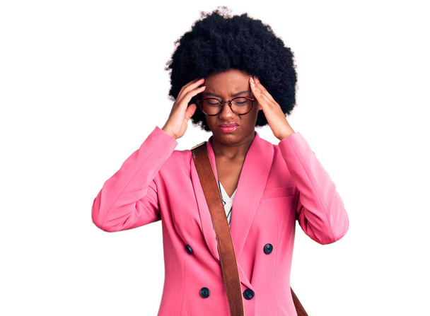 Mujer afroamericana joven que usa ropa de negocios y bolsa de cuero que sufre de dolor de cabeza desesperada y estresada porque el dolor y la migraña. manos en la cabeza.  - Foto, Imagen