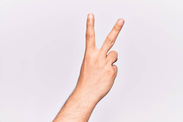 Close up de mão de jovem caucasiano sobre fundo isolado contando número 2 mostrando dois dedos, gesticulando vitória e símbolo vencedor  - Foto, Imagem
