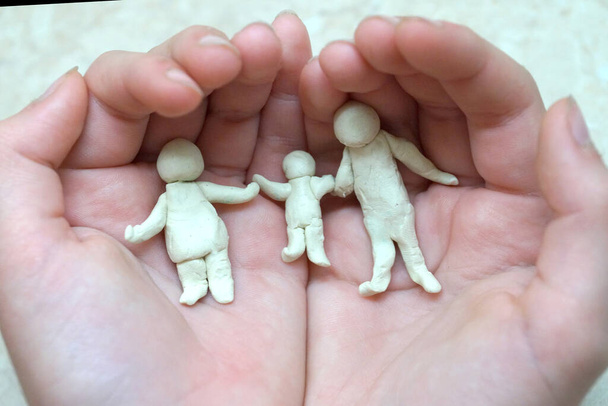 figuras de plastilina de un hombre, una mujer y un niño en manos de niños, encarnando la protección y preservación de los valores familiares - Foto, Imagen