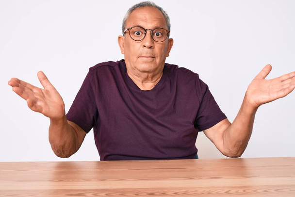 Senior handsome man with gray hair wearing casual clothes and glasses clueless and confused with open arms, no idea and doubtful face.  - Photo, Image