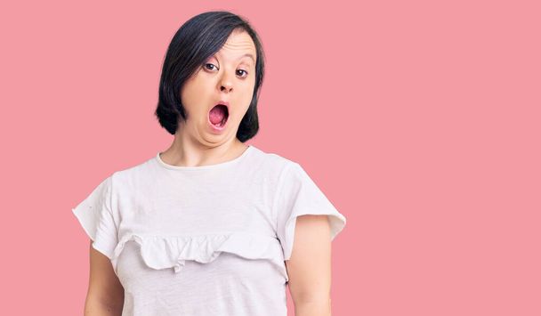Bruneta žena s Downovým syndromem na sobě ležérní bílé tričko strach a šok s překvapením a užaslý výraz, strach a vzrušený obličej.  - Fotografie, Obrázek