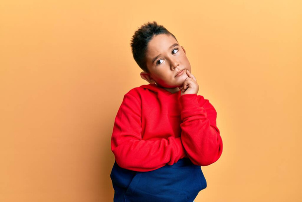 Little boy hispanic kid wearing casual sweatshirt serious face thinking about question with hand on chin, thoughtful about confusing idea  - Foto, imagen
