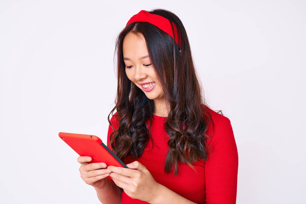 Young beautiful chinese girl holding touchpad looking positive and happy standing and smiling with a confident smile showing teeth  - Fotografie, Obrázek