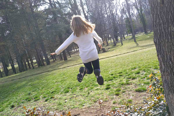 fille sautant dans le parc par une journée ensoleillée, vue arrière - Photo, image