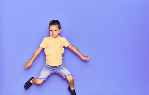 Очаровательный ребенок в повседневной одежде прыгает через изолированный фиолетовый фон - Фото, изображение