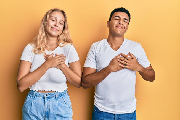 Ein junges Paar in lässigem weißem T-Shirt, das mit geschlossenen Augen und dankbarer Geste auf der Brust lächelt. Gesundheitskonzept.  - Foto, Bild