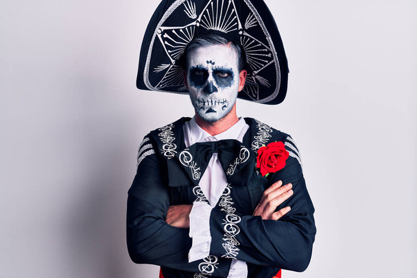 Молодой человек, одетый в мексиканский день мертвого костюма над белым скептиком и нервным, неодобрительным выражением лица со скрещенными руками. отрицательный человек.  - Фото, изображение