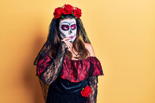 Young woman wearing day of the dead costume over yellow looking stressed and nervous with hands on mouth biting nails. anxiety problem.  - Photo, Image