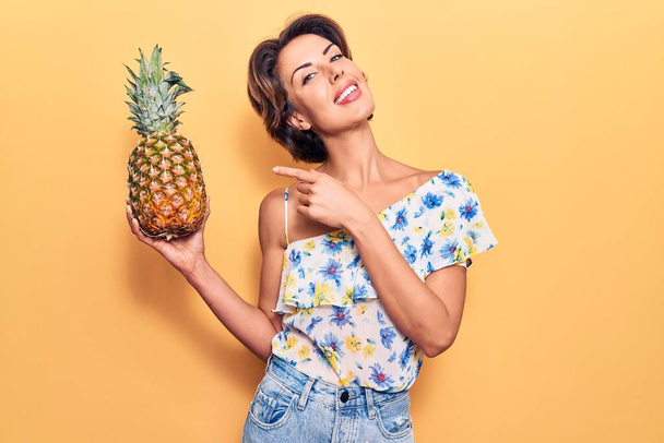 Fiatal gyönyörű nő kezében ananász mosolyog boldog rámutatva a kezét és ujját  - Fotó, kép