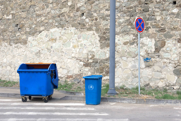 Blue plastic trash bins and road sign by the stone wall background. - Photo, Image