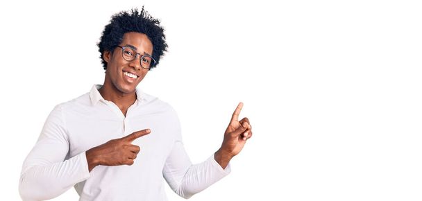 Beau Afro-Américain aux cheveux afro portant des vêtements décontractés et des lunettes souriantes et regardant la caméra pointant avec deux mains et doigts sur le côté.  - Photo, image