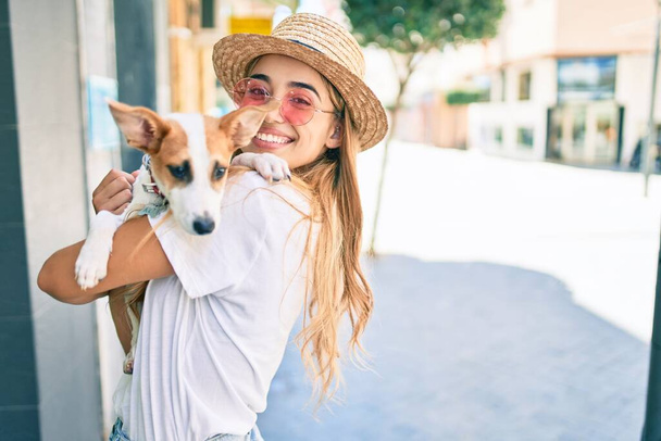 Young beautiful blonde woman hugging and cuddling puppy dog outdoors - Photo, Image