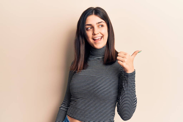 Joven hermosa chica vistiendo casual rayas camiseta apuntando pulgar hacia el lado sonriendo feliz con la boca abierta  - Foto, imagen