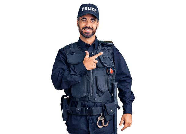 Nuori latinomies yllään poliisi univormu iloinen hymy kasvoillaan osoittaa käsi ja sormi jopa puolelle onnellinen ja luonnollinen ilme  - Valokuva, kuva
