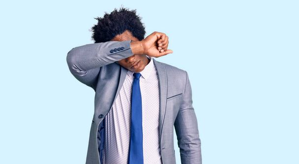Handsome african american man with afro hair wearing business jacket covering eyes with arm, looking serious and sad. sightless, hiding and rejection concept  - Foto, Imagem