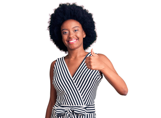 Fiatal afro-amerikai nő alkalmi ruhát visel, boldog hüvelykujjával felemeli a kezét. jóváhagyása kifejezés nézi a kamera mutatja siker.  - Fotó, kép