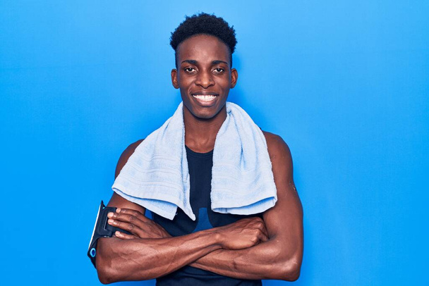 Junger afrikanisch-amerikanischer Mann in Sportbekleidung und Handtuch mit glücklichem Gesicht und verschränkten Armen, die in die Kamera schauen. positive Person.  - Foto, Bild