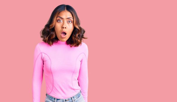Young beautiful mixed race woman wearing pink shirt scared and amazed with open mouth for surprise, disbelief face  - Photo, Image