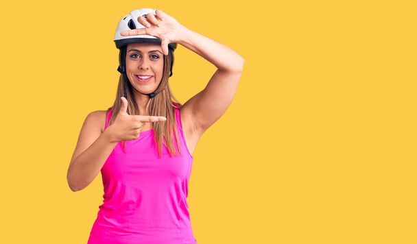 Young beautiful woman wearing bike helmet smiling making frame with hands and fingers with happy face. creativity and photography concept.  - Zdjęcie, obraz