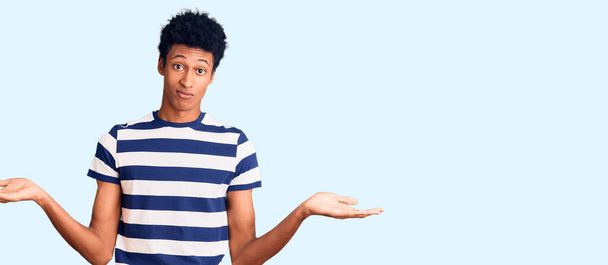 Jeune homme afro-américain portant des vêtements décontractés expression désemparée et confuse avec les bras et les mains levées. concept de doute.  - Photo, image