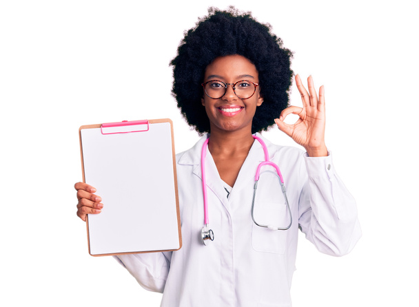 Jonge Afro-Amerikaanse vrouw draagt dokter stethoscoop houden klembord doet ok teken met de vingers, glimlachende vriendelijke gebaar uitstekend symbool  - Foto, afbeelding