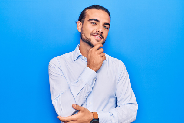 Young handsome man wearing business clothes smiling looking confident at the camera with crossed arms and hand on chin. thinking positive.  - Photo, image