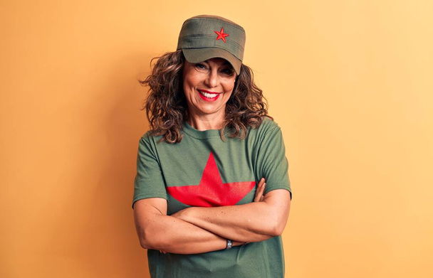 Středního věku brunetka žena v tričku a čepici s červenou hvězdou symbol komunismu šťastný obličej usmívá se zkříženýma rukama se dívá do kamery. Pozitivní osoba. - Fotografie, Obrázek