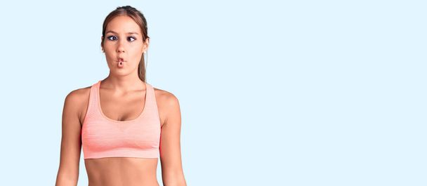 Young beautiful hispanic woman wearing sportswear making fish face with lips, crazy and comical gesture. funny expression.  - Foto, Imagem