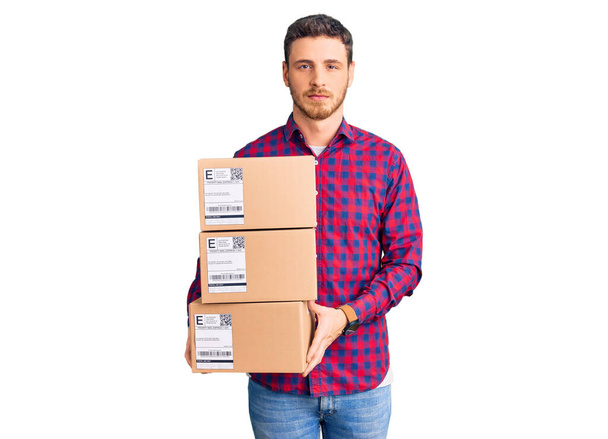 Handsome young man with bear holding delivery packages thinking attitude and sober expression looking self confident  - Photo, Image