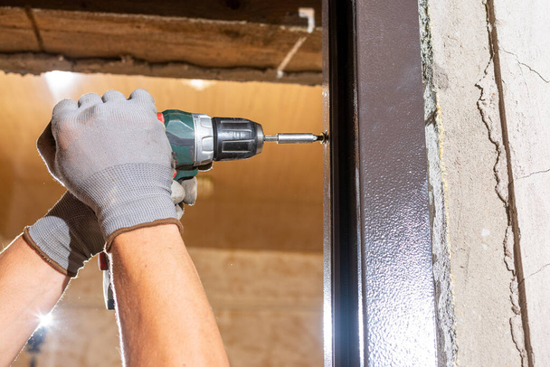 The carpenter drills holes in the wall and the metal door frame with a drill, later screws the screws and fastens the door frame to the wall.2020 - Foto, imagen