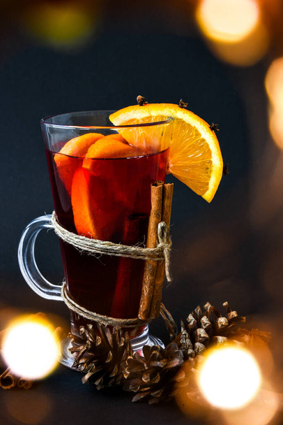 Mulled wine Hot christmas drink with spices on a dark background. Orange slices, cinnamon sticks, christmas cones, bright bokeh. Christmas light. Holiday atmosphere, Rustic style. The idea for creating greeting cards - Zdjęcie, obraz