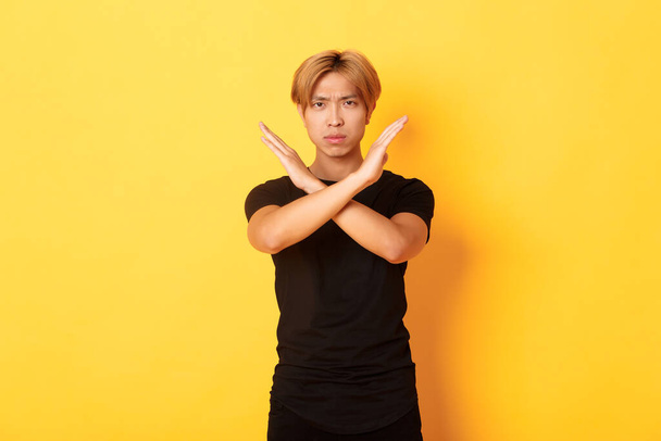 Retrato de desapontado franzindo a testa asiático homem, fazendo cruz gesto para parar algo ruim, de pé fundo amarelo - Foto, Imagem