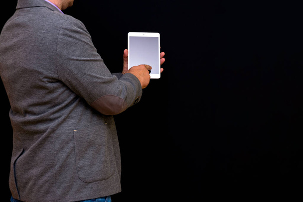 Geschäftsmann mittleren Alters hält Tablet-PC mit leerem Bildschirm auf schwarzem Hintergrund und zeigt ihn. - Foto, Bild