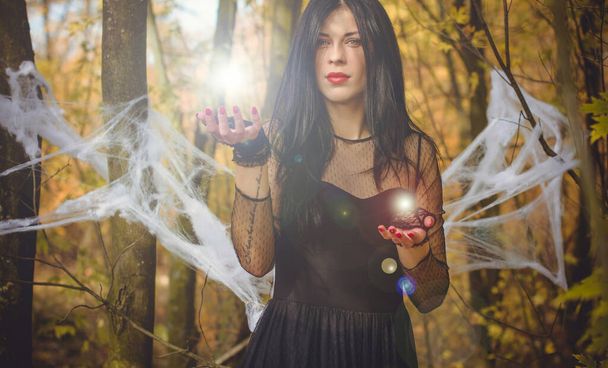 Halloween heks in een donker bos. Mooie jonge vrouw in heksen moderne jurk. Halloween kunst ontwerp. Donker thema voor Halloween Concept - Foto, afbeelding