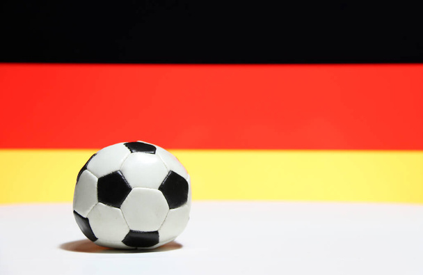 黒い赤とドイツ国旗の背景の黄色の色を持つ白い床の上の小さなサッカー。スポーツの概念. - 写真・画像