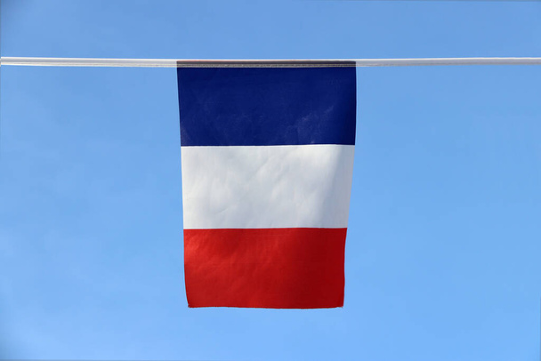 Mini bandeira de trilho de tecido da França é uma bandeira tricolor com três faixas verticais coloridas de azul branco e vermelho, pendurado no pano de corda no fundo do céu azul. - Foto, Imagem