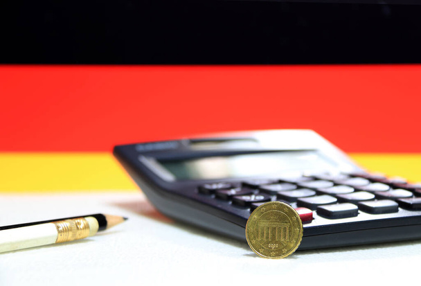 Deset německých eurocentů na lícové straně na bílé podlaze s černou kalkulačkou a tužkou, pozadí německých vlajek, koncept financí. - Fotografie, Obrázek