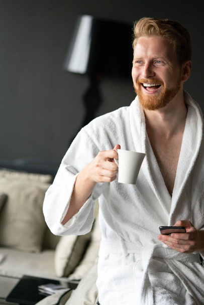 Young man in bathrobe drinking coffee at hotel, spa center. - Fotografie, Obrázek