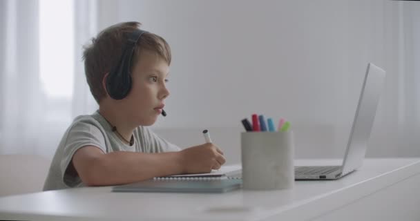 家庭での学校の少年のためのeラーニング、子供はノートパソコンでウェビナーを表示し、コピーブック、語学研修で書いています - 映像、動画