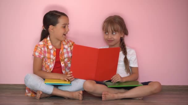 Pembe arka planda kitap okuyan iki küçük kız. - Video, Çekim